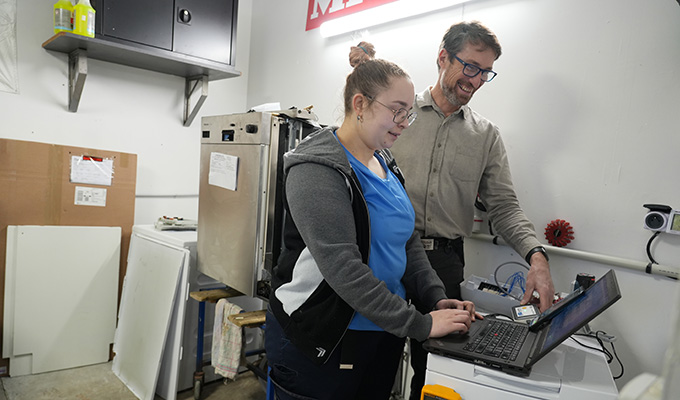 Deux personnes souriantes devant un ordinateur dans un atelier